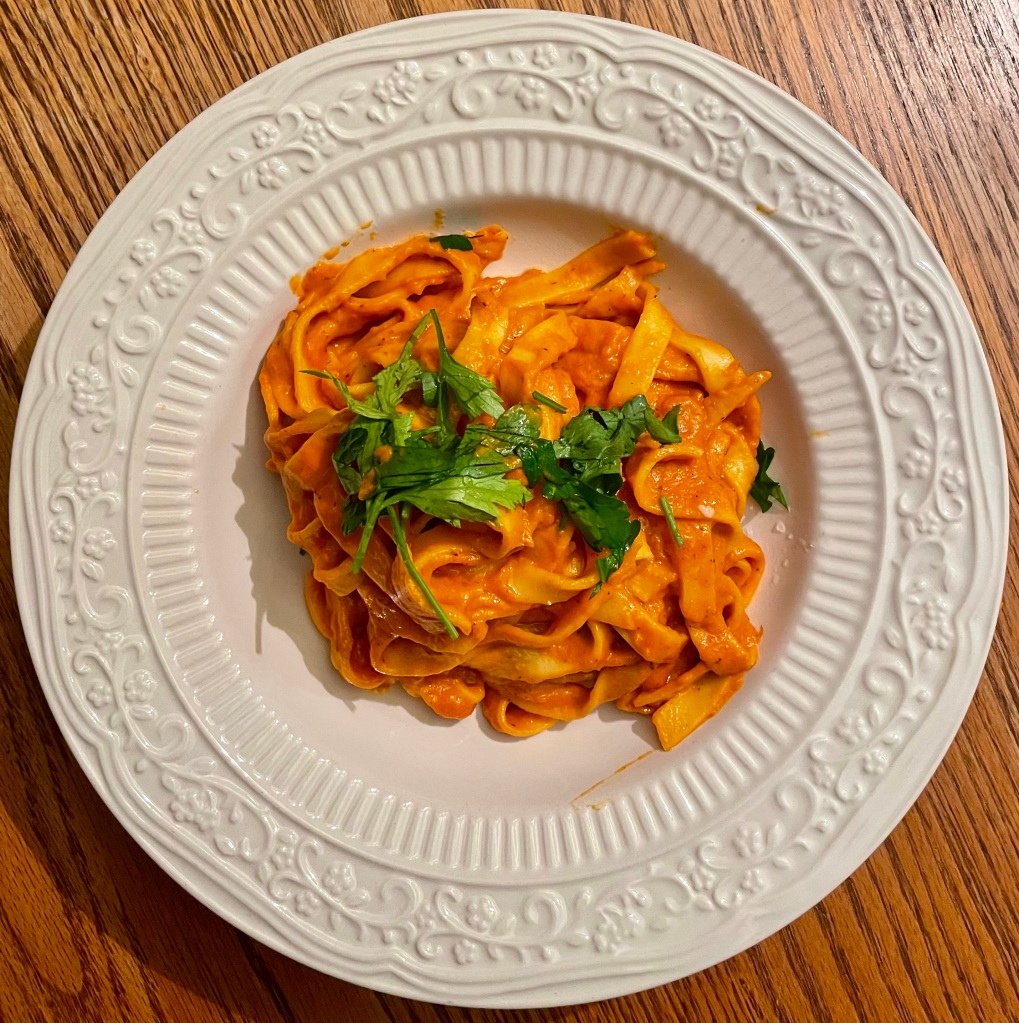 image description: bowl of homemade fettuccine pasta with homemade vodka sauce and fresh parsley on top. 