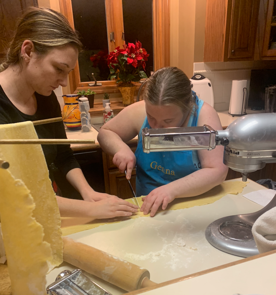 image description: Lauren holds the flat dough in place while I cut it in half so that the pasta is a shorter length. 
