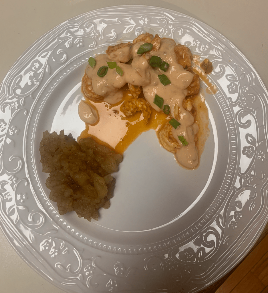 image description: orange firecracker shrimp with a creamy orange sauce and scallions on top, and homemade applesauce on a white plate.