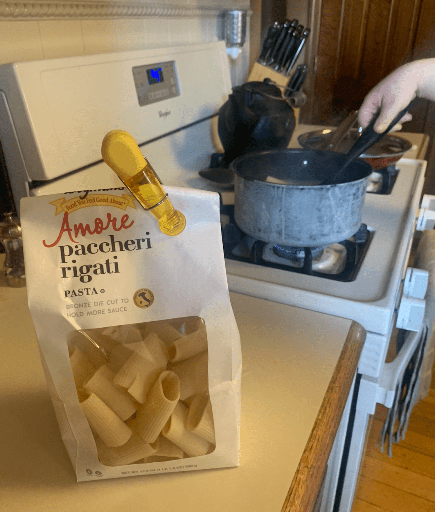 alt text: a bag of pasta in front a boiling pot of water on the stove.