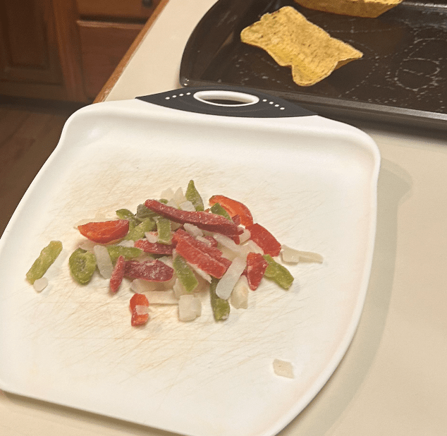 alt text: a mix of frozen peppers and onions on the cutting board.