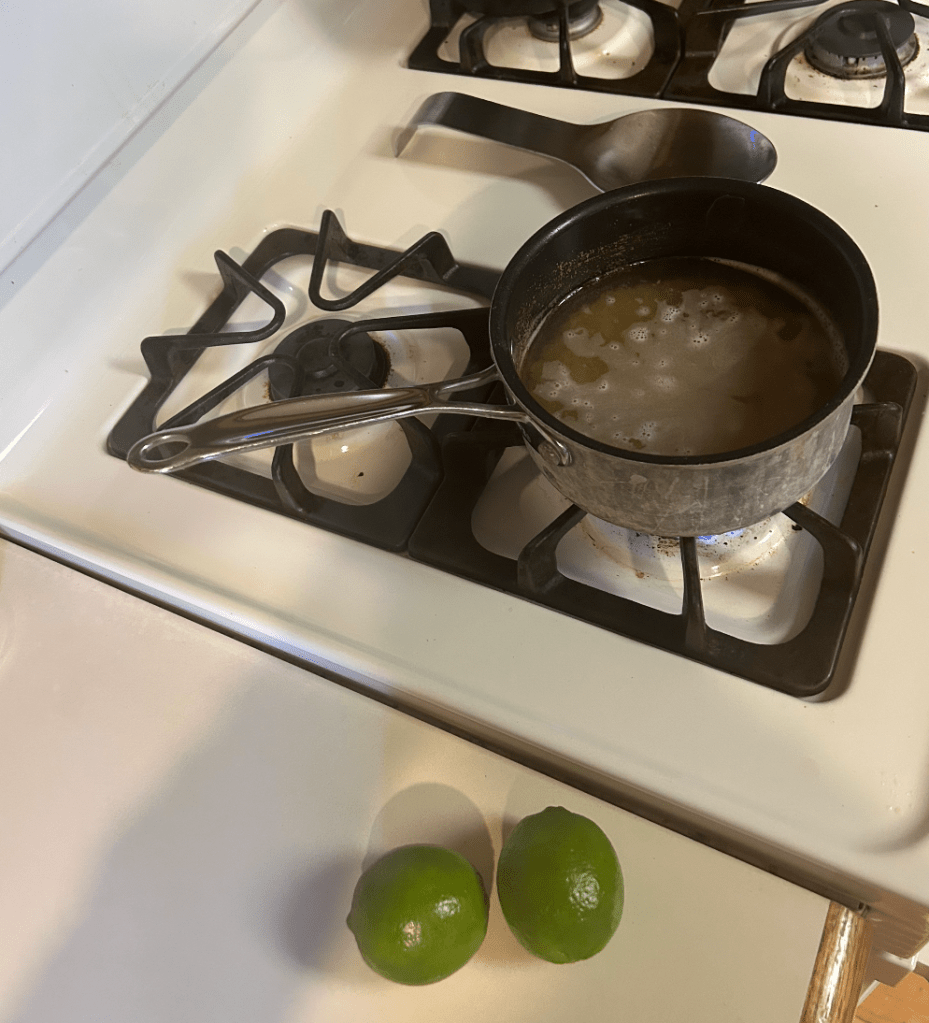 alt text: the rice cooking in a pot on the stove next to two limes on the counter