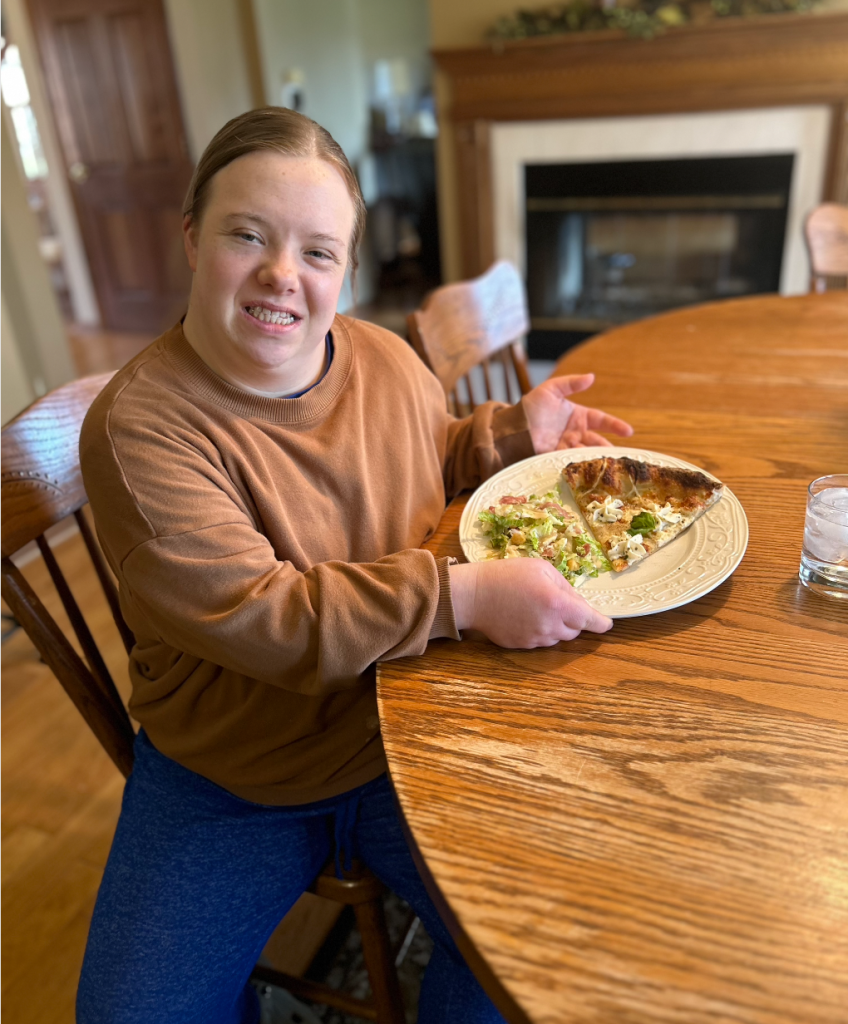 I am sitting at the table with my plate of food: a piece of pizza and salad.